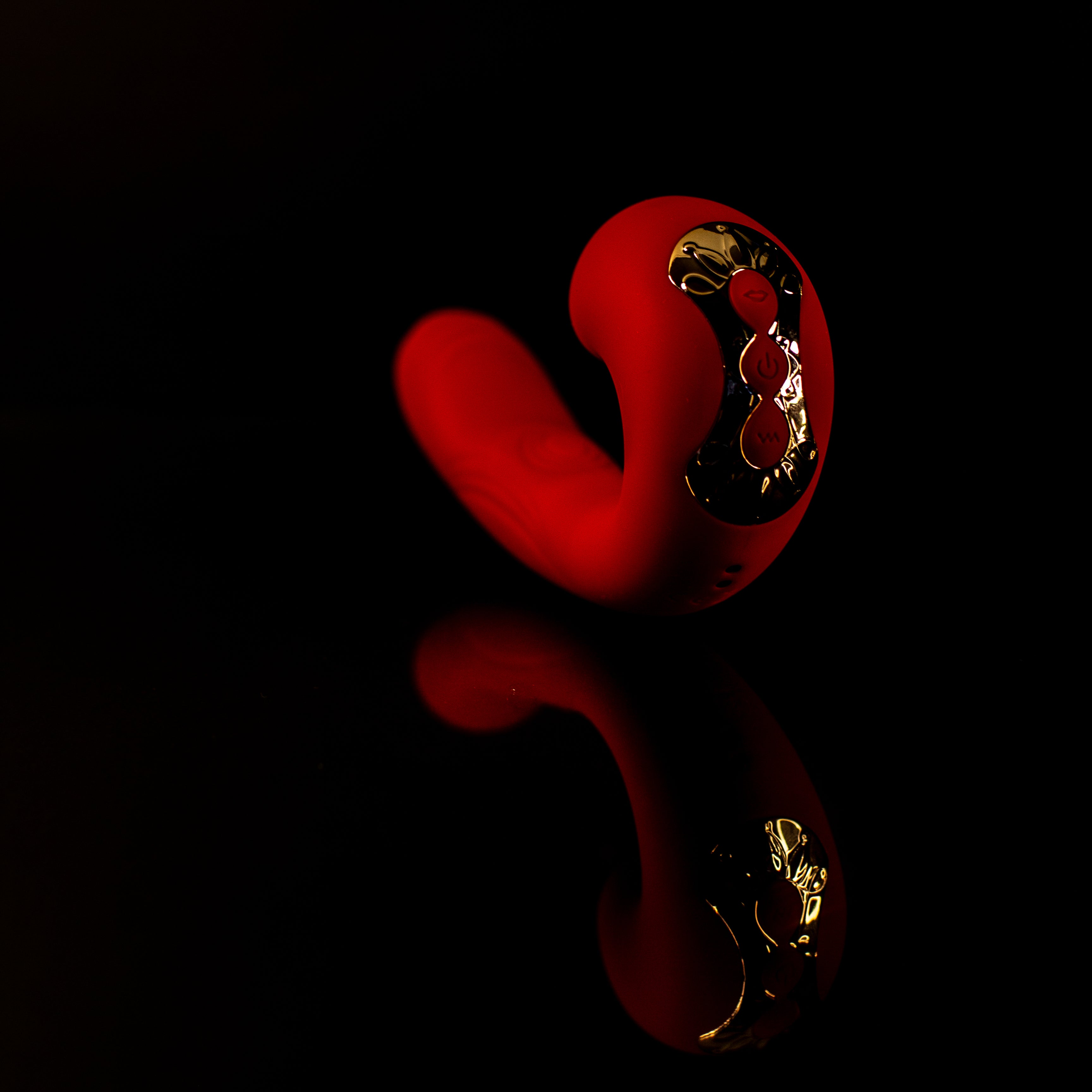 Red pleasure toy with gold detailing on a black background showing reflection of product
