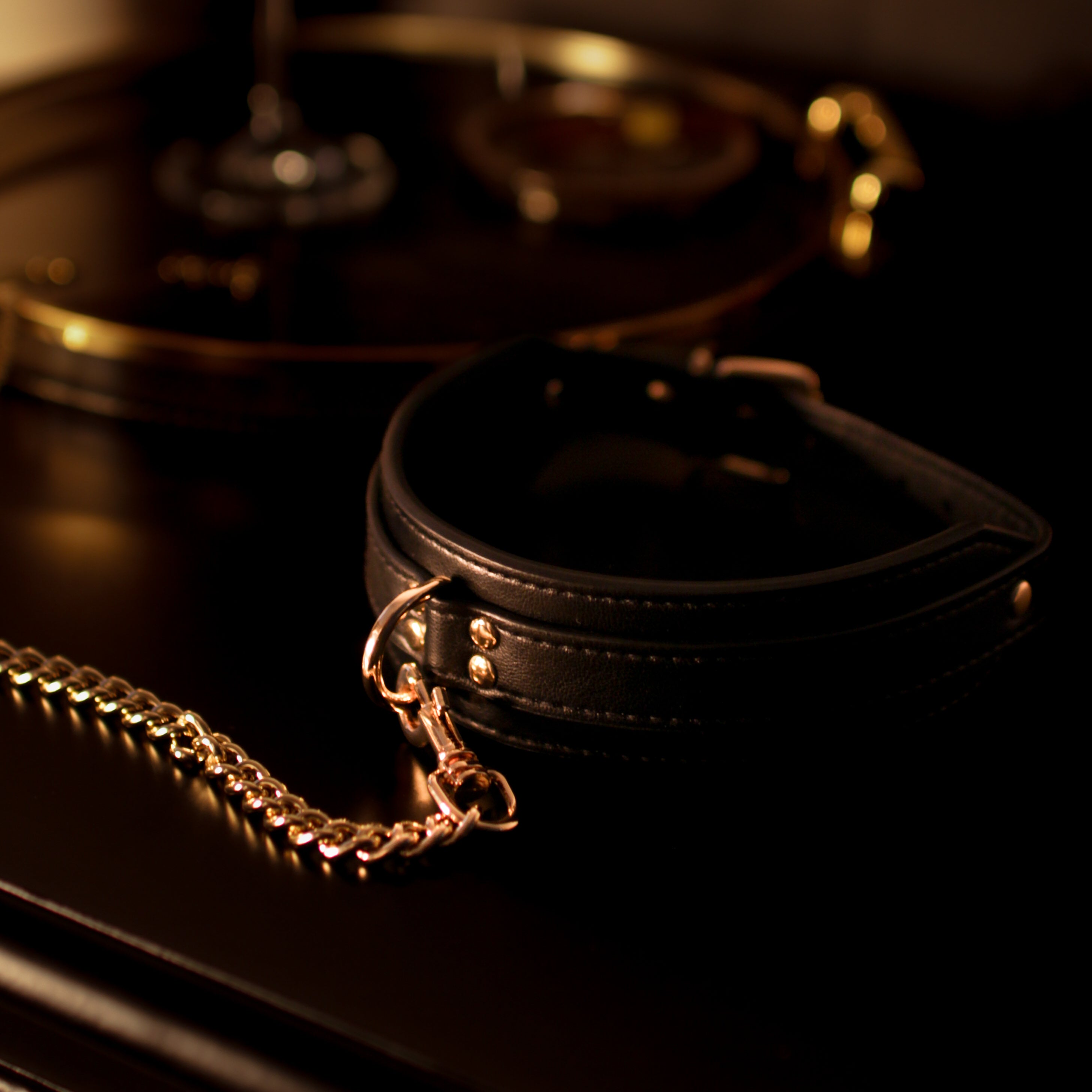 Black leather collar with gold chain on a dark surface