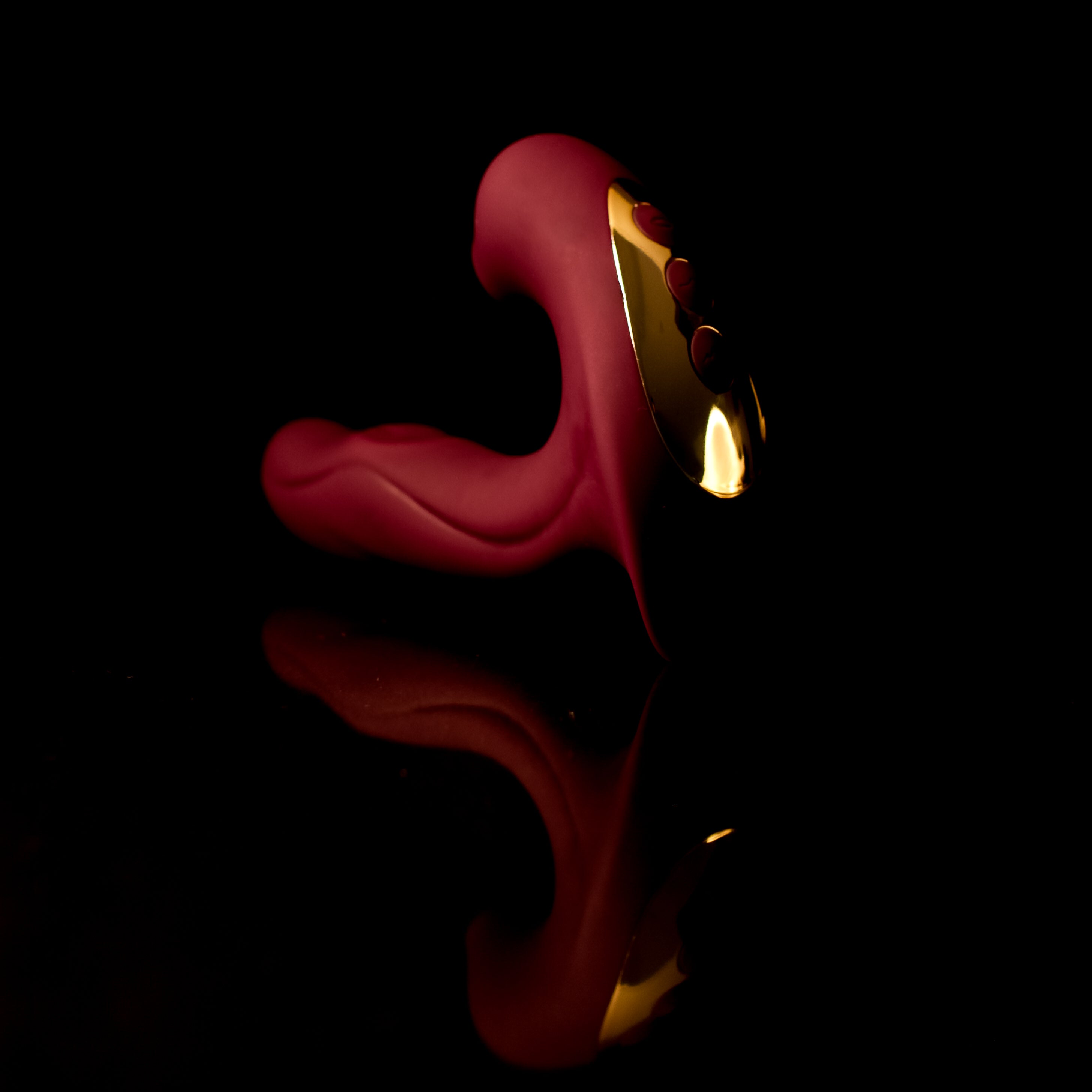 Red pleasure toy with gold hardware on a black background