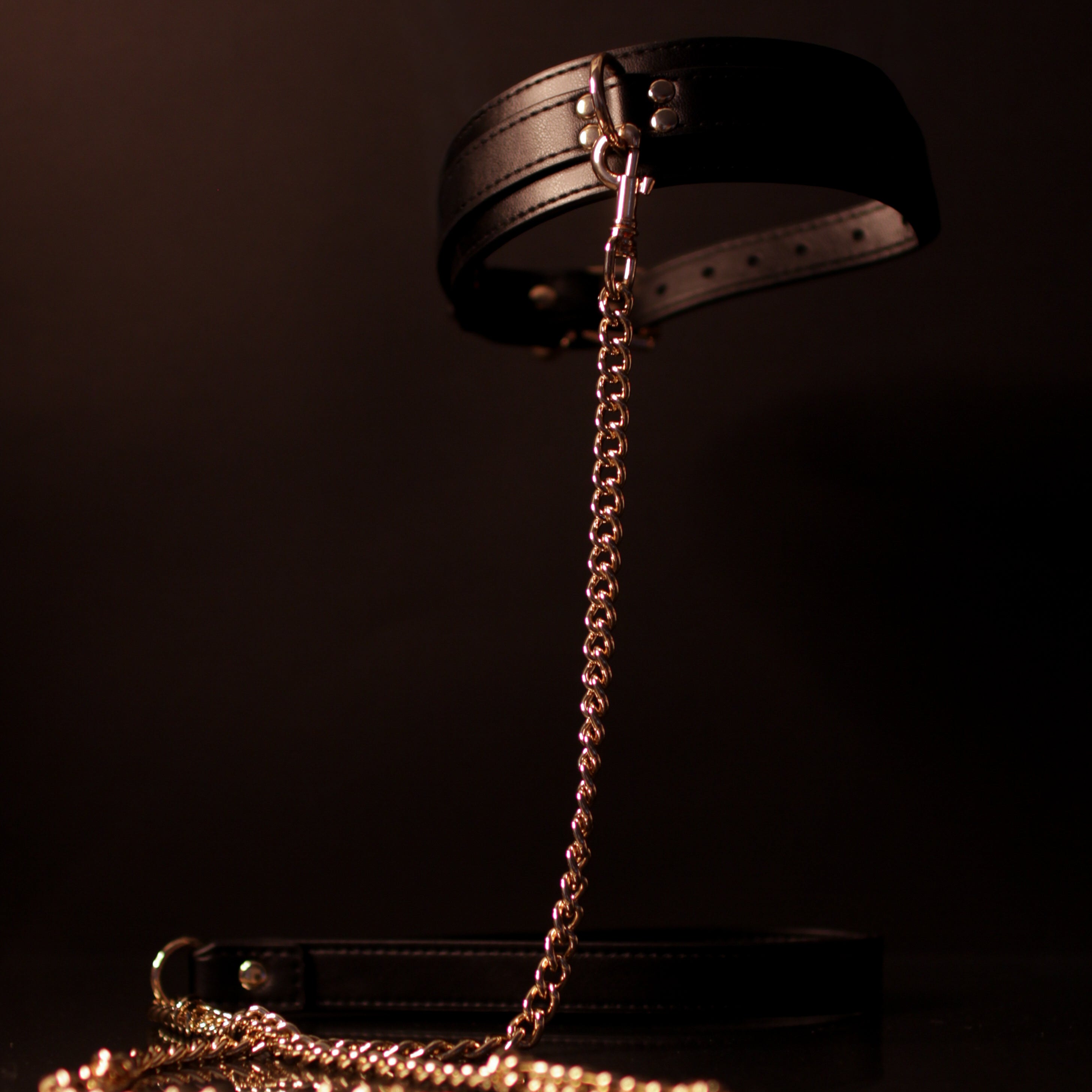 Black leather collar with a gold chain floating in the air on a dark background