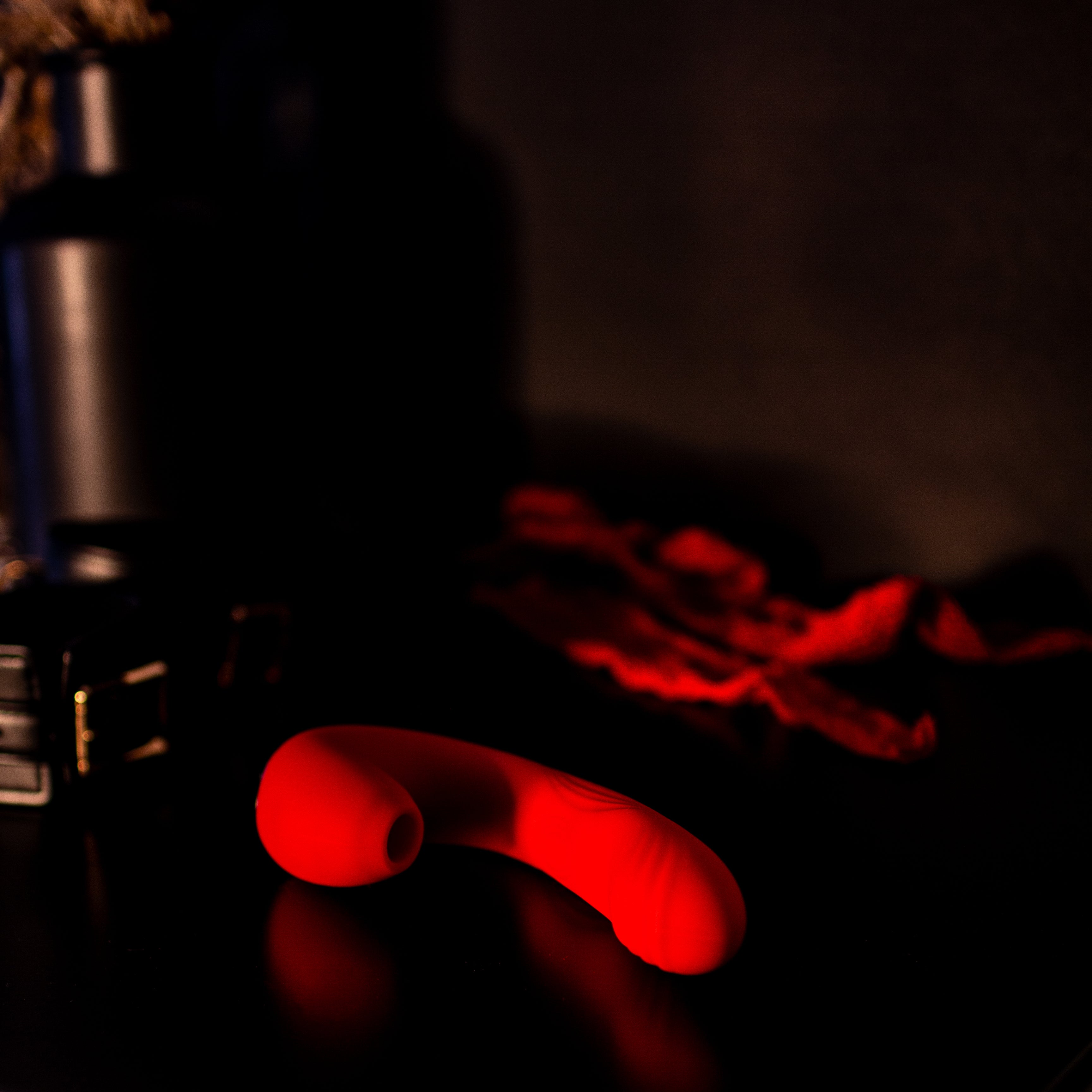 Red pleasure toy on a dresser in dark room.